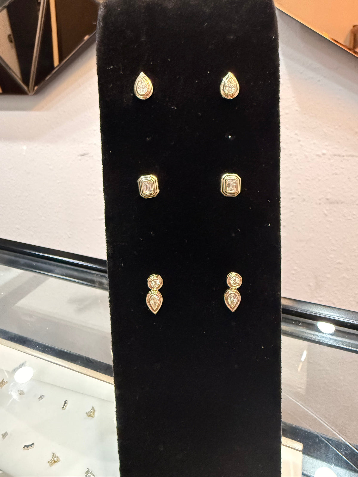 The Karat Concierge Gatsby Stud earrings in 14K yellow gold with emerald-cut diamonds on a black velvet display stand.