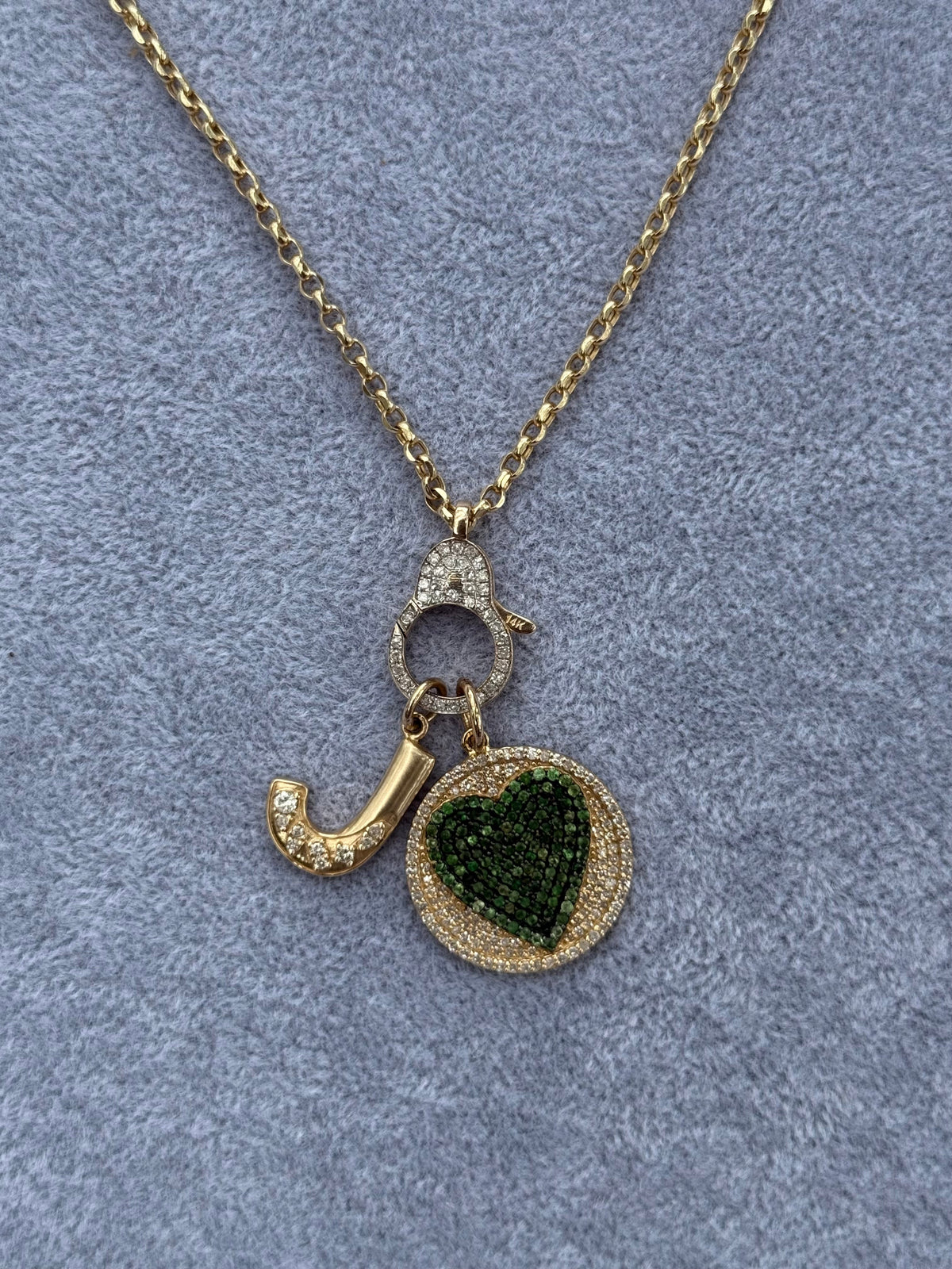The Karat Concierge round pendant featuring a pavé emerald heart, diamond accents, and a gold chain with a push lock.