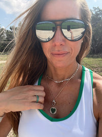 The Karat Concierge round pendant with pavé emerald heart and diamonds on a gold chain worn by a woman outdoors.