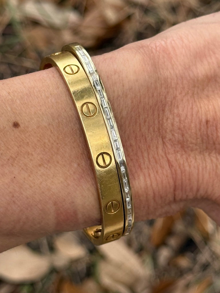 The Karat Concierge yellow gold screw-motif bangle stacked with a channel-set baguette diamond bangle on a wrist.