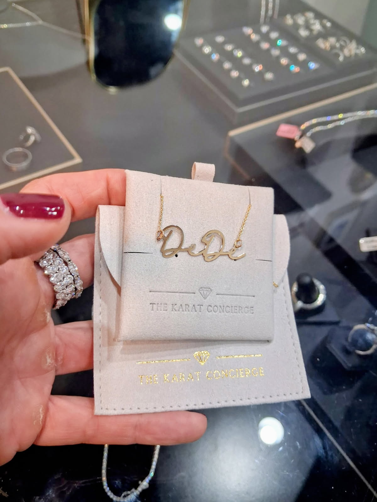 The Karat Concierge custom 14K yellow gold name necklace featuring elegant script lettering on a beige display card.
