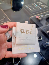 The Karat Concierge custom 14K yellow gold name necklace featuring elegant script lettering on a beige display card.