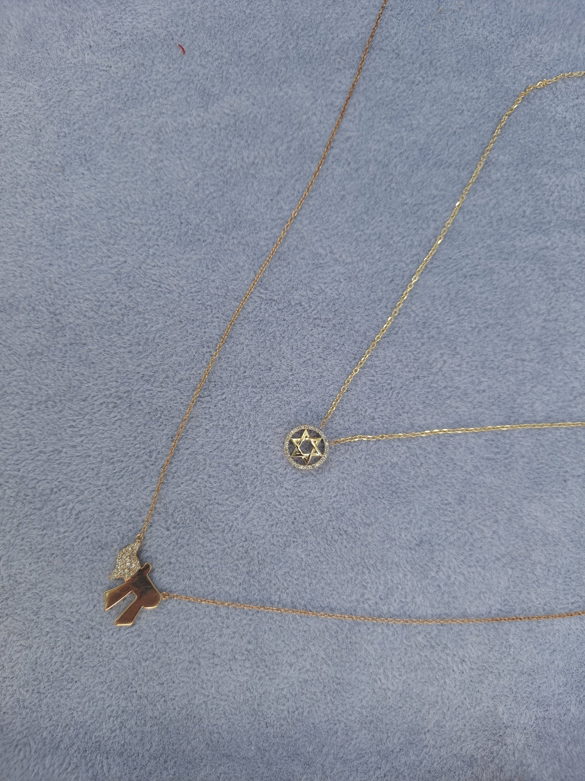 The Karat Concierge 14K yellow gold Star of David necklace with diamond accents on a light blue velvet background