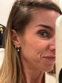 The Karat Concierge 14K yellow gold huggie earrings with marquise diamond drops worn on a woman's ear