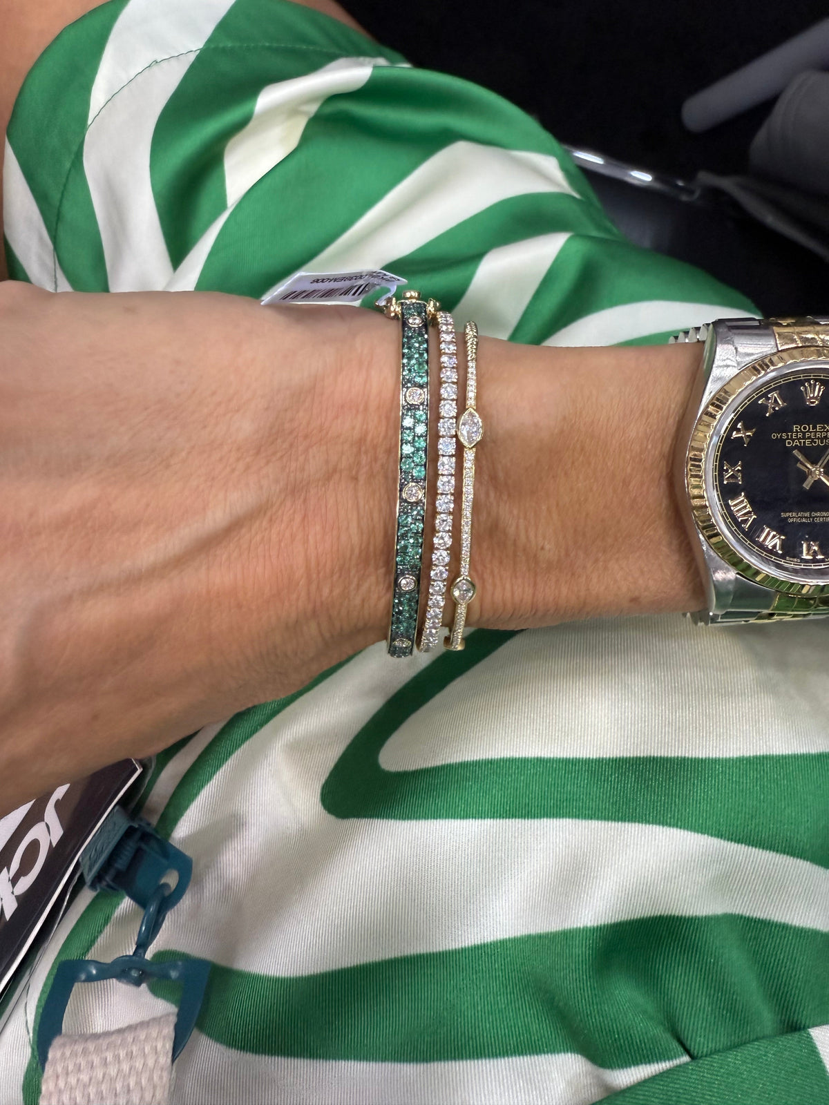 The Karat Concierge Pave Muse bangle with green gemstones and bezel-set diamonds stacked with gold diamond bracelets.