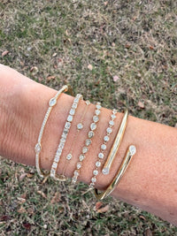 The Karat Concierge 14K yellow gold hinged cuff bangle with two pear-shaped bezel-set diamonds on a wrist stack
