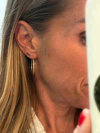 The Karat Concierge 14K yellow gold curved bar earrings featuring three round blue sapphires worn on an earlobe.