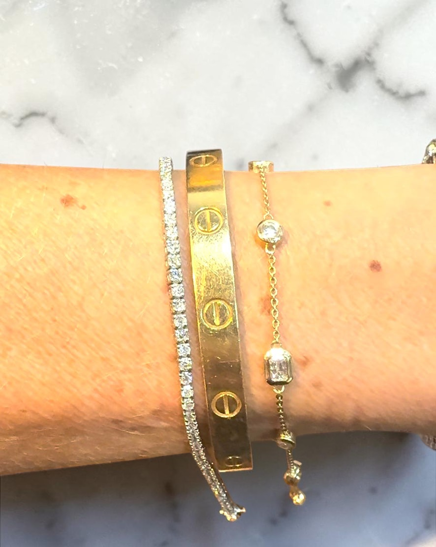 The Karat Concierge Sloane bezel set 14K yellow gold bracelet with natural diamonds worn on a wrist with other bangles