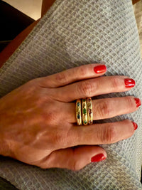 The Karat Concierge stacked 14KT yellow gold donut rings featuring oval-cut colorful gemstones on a woman's hand.