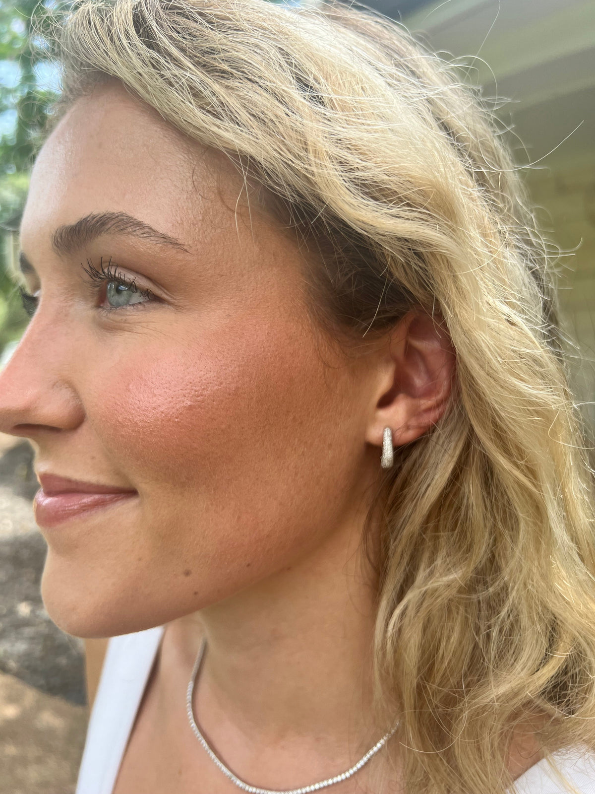 The Karat Concierge 14K white gold huggie earrings with pave natural diamonds worn by a blonde woman